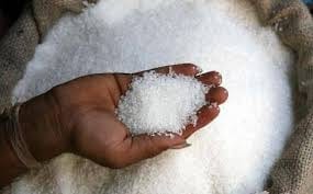 A handful of white granulated sugar lifted from an open jute sack of bulk sugar